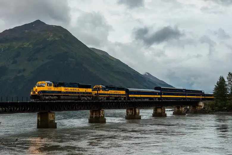 Trem azul e amarelo do Alaska Railroad cruzando ponte sobre rio