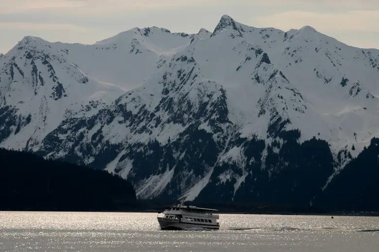 Barco navegando na Resurrection Bay diante de montanhas nevadas, em Seward