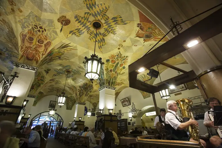 Salão de cervejaria histórica de Munique, com teto abobadado pintado e música ao vivo