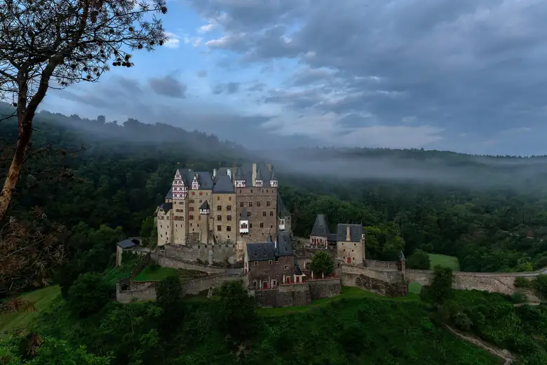 Burg Eltz emergindo da floresta sob a neblina da manhã
