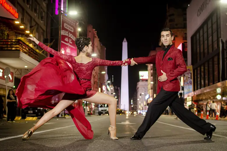 Casal de tango dançando à noite na avenida Corrientes, com o Obelisco ao fundo