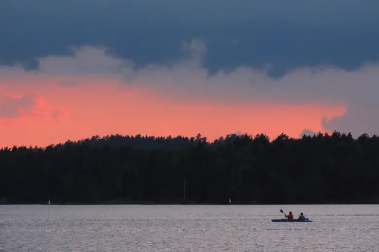 Canoa cruzando um lago finlandês sob o céu rosado do entardecer