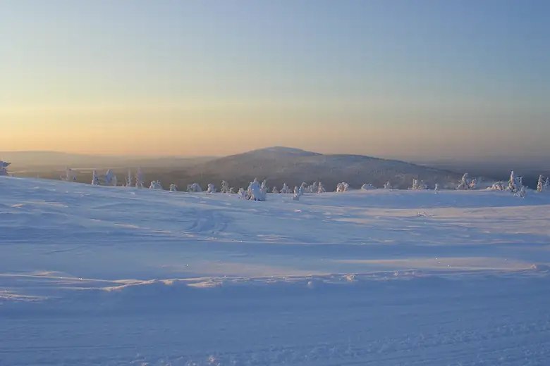 Monte nevado da Lapônia ao entardecer com árvores carregadas de neve