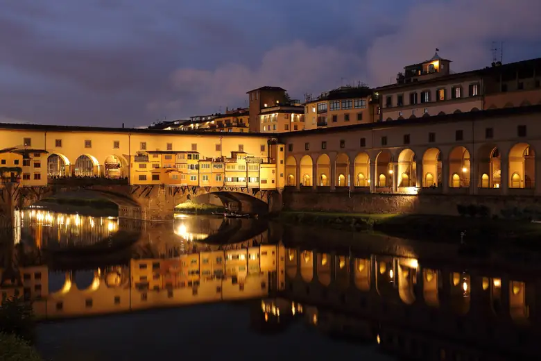 Ponte Vecchio iluminada refletida no rio Arno à noite