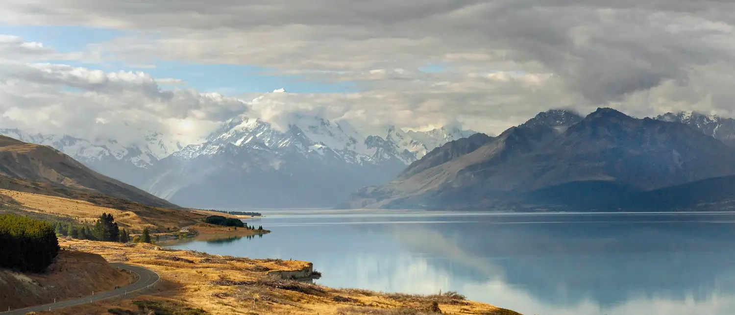 Estrada margeando o lago Pukaki, turquesa, com Aoraki/Mount Cook ao fundo