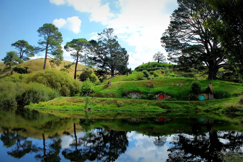 Tocas de hobbit coloridas refletidas no lago em Hobbiton, Matamata
