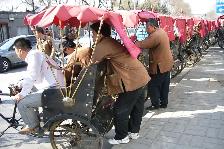 Fila de rickshaws com capotas vermelhas à espera de passageiros em Pequim