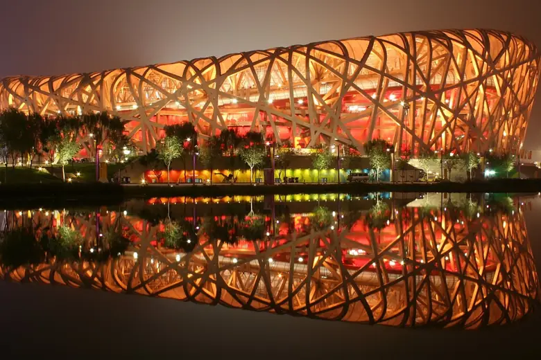 O estádio Ninho de Pássaro iluminado refletido na água à noite