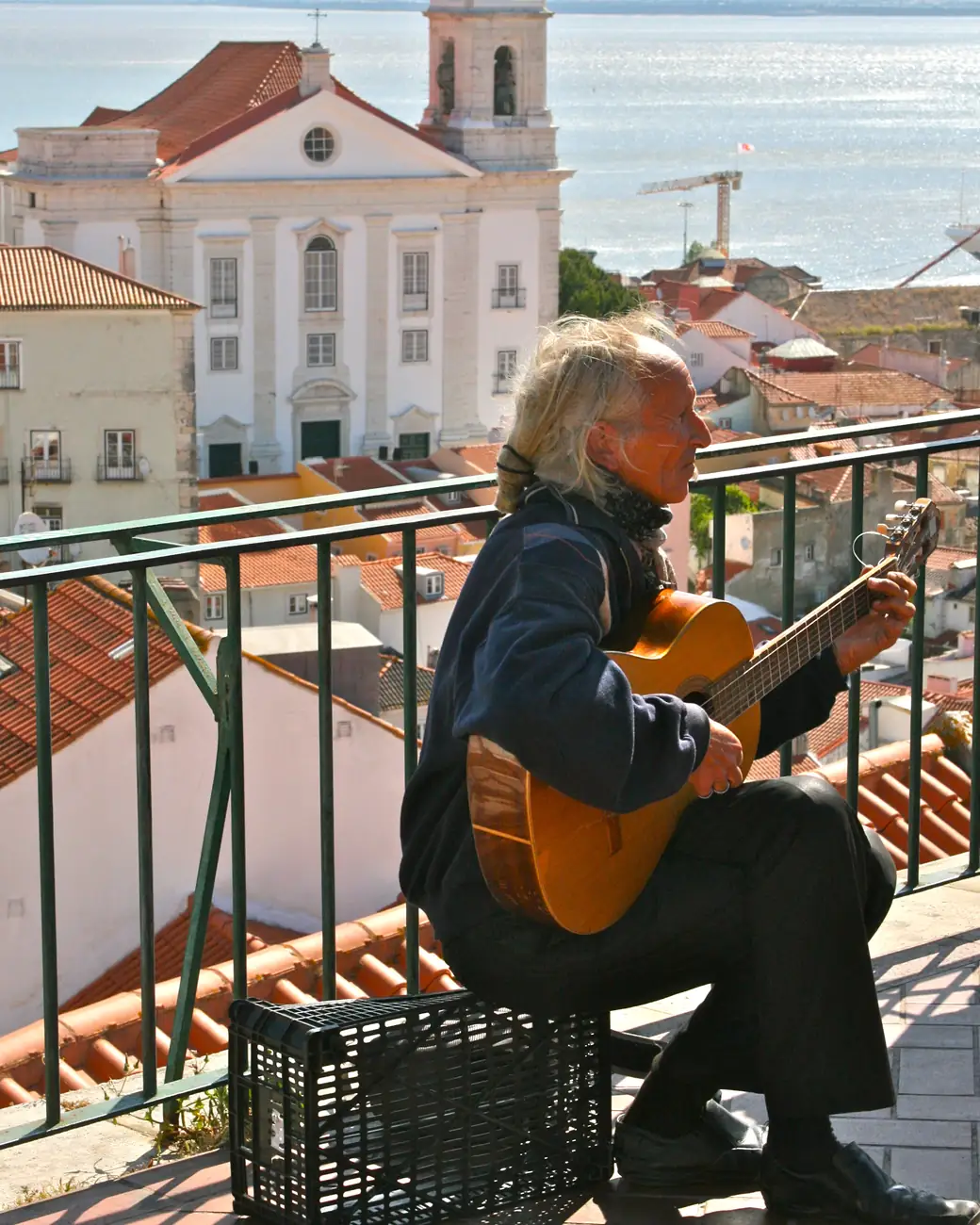 Guitarrista diante do casario de Alfama e do rio Tejo, em Lisboa