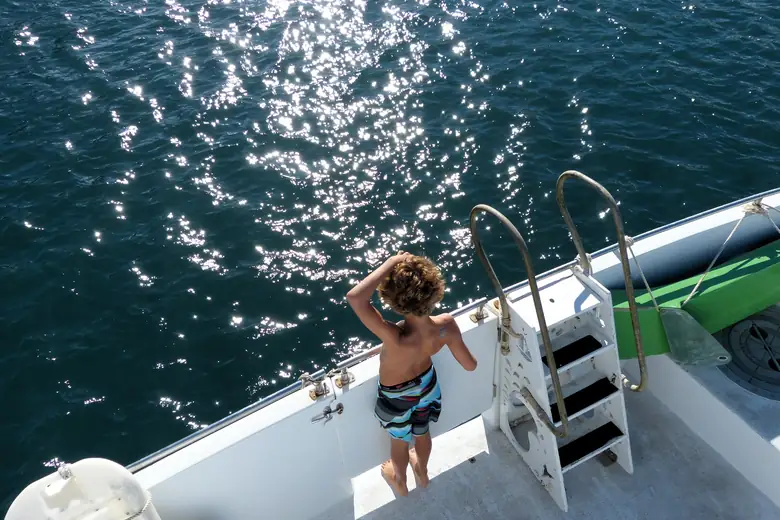 Menino observando o mar brilhante do deck de um barco