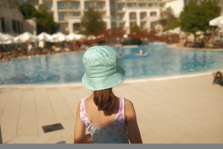 Menina de chapéu observando a piscina de um resort