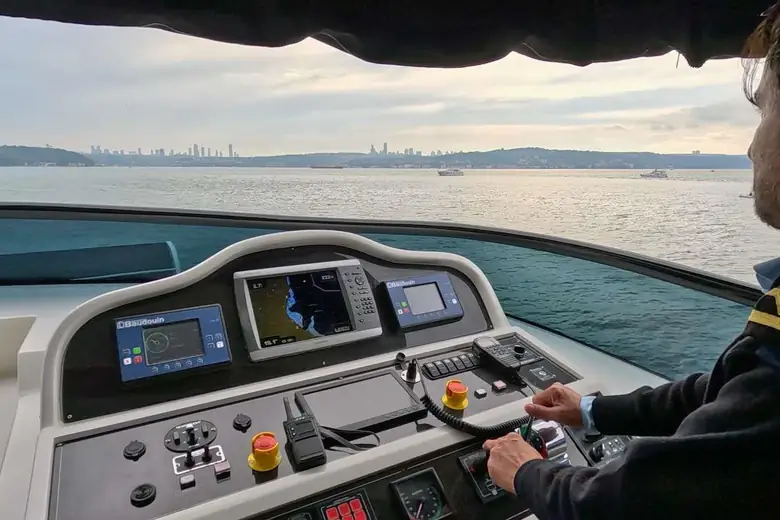 Capitão ao timão do iate navegando o Bósforo, com Istambul ao fundo